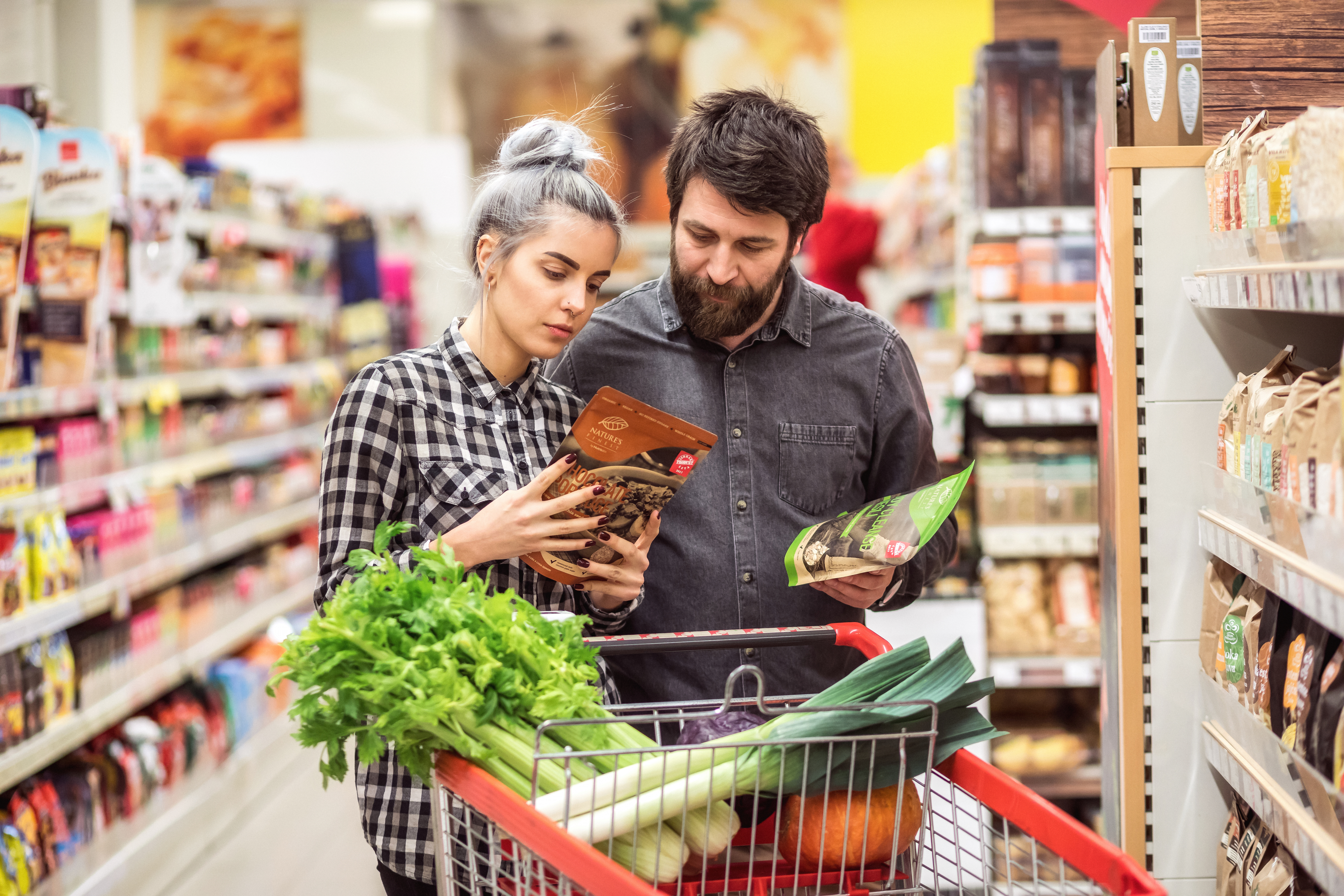 Zwei Personen checken Angaben auf Lebensmittelverpackungen im Supermarkt.