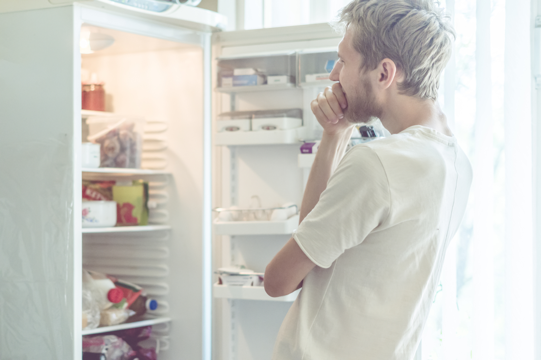 Mann blickt ratlos in offenen Kühlschrank