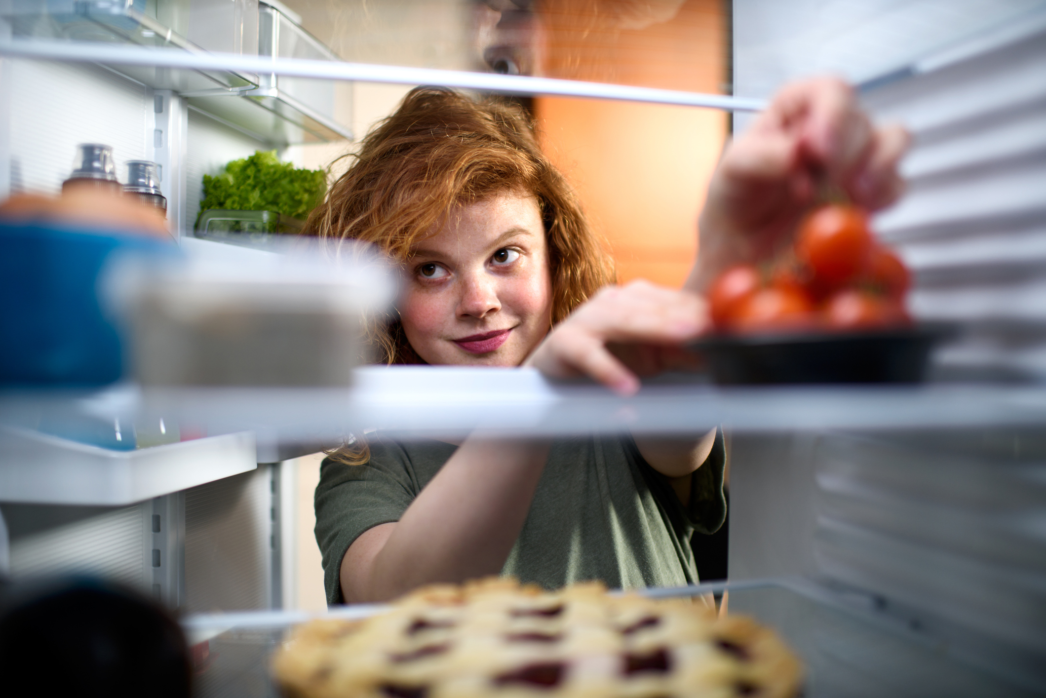 Junge Frau greift nach Tomaten im Kühlschrank