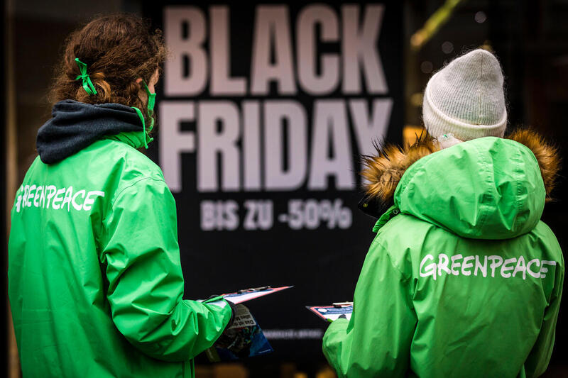 Zwei Greenpeace Aktivistinnen stehen vor einem Black Friday Plakat.