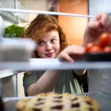 Junge Frau greift nach Tomaten im Kühlschrank